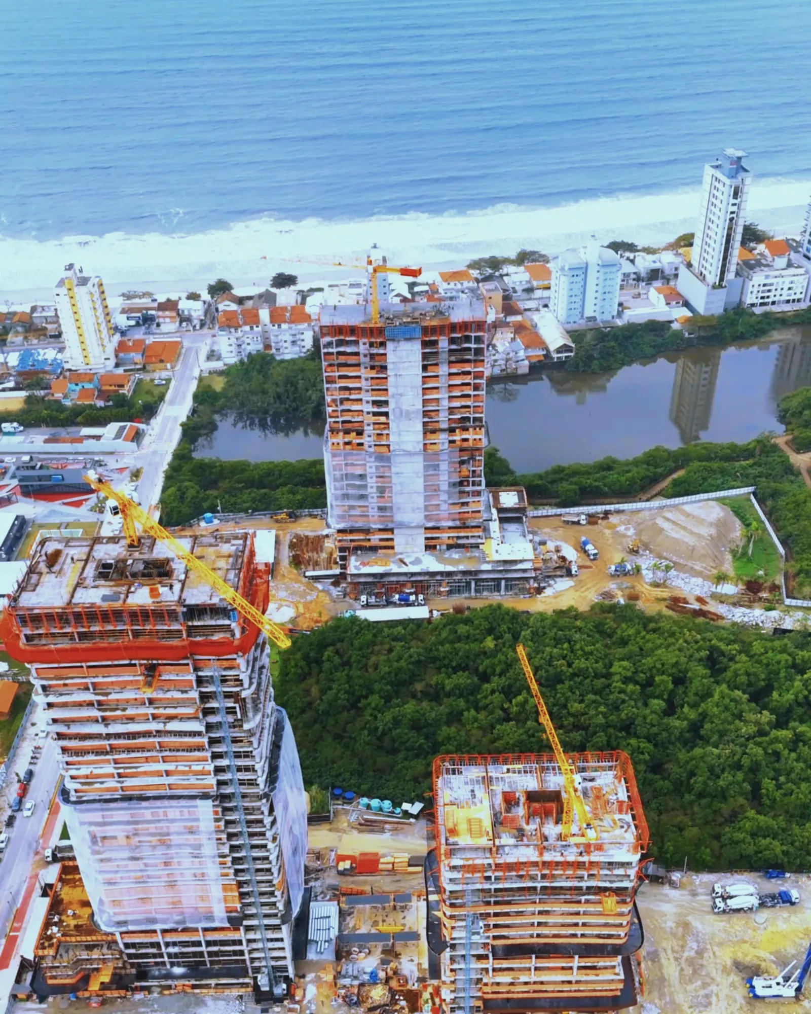 Vista aérea das torres do Lagom Perequê em construção, entre a mata do parque, a lagoa e o mar de Porto Belo